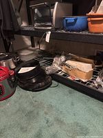 Shelving with pots, black non-stick pans, blue and orange plastic containers, some small electronics on top shelf