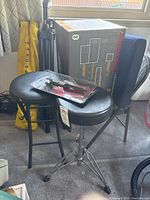 Two black round stools (drum throne and bar stool), yellow carrying bag for tripod, black folding mesh chair, Peavey mixer box