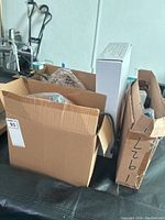 Cardboard boxes containing boxed and loose items on a table with a walker in background
