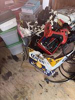 Wide shot showing the cordless drill, charger, assorted hand tools, and plastic storage bins stacked nearby.