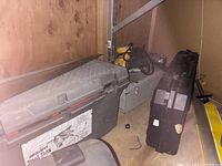 Photo showing multiple toolboxes and a yellow DeWalt drill on a wooden shelf, dusty and used.