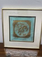 Framed brass artwork showing a dragon and phoenix design in a turquoise patina frame with beige mat and gold-tone frame.