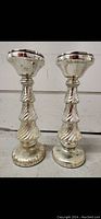Photo showing a pair of silver colored distressed candle holders with a spiral and fluted design, each approximately 31 cm tall, in a rustic style.