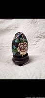 Front view of the Chinese cloisonné egg showing floral enamel decoration and wooden base.