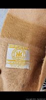 Close-up photo of the original Hudson's Bay Company sewn label on the light brown wool blanket, showing the label details including the company's seal and 'Made in England' text.