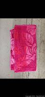 Folded pink Hawaiian themed beach towel with large floral and leaf pattern, laying on concrete background.