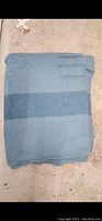 Folded light blue wool blanket with broad dark blue stripe lying on floor.
