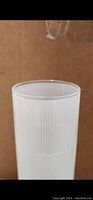 Close-up of top edge of cylindrical white glass vase showing vertical line etched pattern.