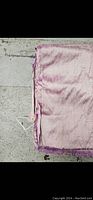 Light pink silk fabric folded with frayed edges visible, laid out on a stone surface.