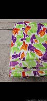 Folded Thai silk fabric with white base and abstract purple, orange, green motifs on textured concrete background
