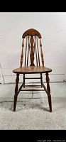 Front view of wooden desk chair showing legs, seat, and backrest with vertical spindles and decorative slat.