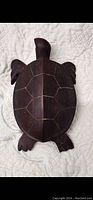 Top view of a solid wood turtle carving placed on a white textured fabric showing carved segment details on the shell and limbs.