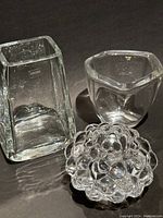 Three clear crystal items: raspberry-patterned crystal votive, small square vase, and rectangular vase with Krosno label