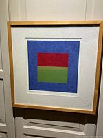 Full view of abstract print framed in blonde wood, showing the geometric composition of red, green rectangles on blue background.