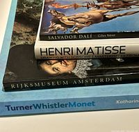 Front spines and covers of four art books, showing titles and authors including 'Dali' by Gilles Néret, Henri Matisse book, Rijksmuseum Amsterdam, and Turner Whistler Monet.