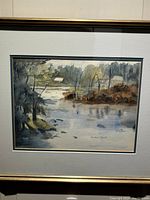 Framed watercolour painting showing a tranquil pond scene, trees, and a house in the distance.