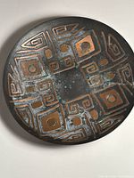 Top-down image showing full decorative brass plate with brutalist geometric relief design and patina.