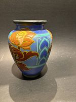 Front and side view of Dutch Antique Gouda vase with colorful floral relief design on blue background and visible chip repairs on rim.