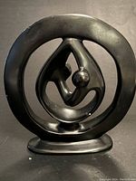 Front view of black abstract sculpture with circular frame and inner curved elements including a spherical feature.