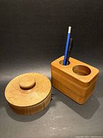 Round wooden lidded container and rectangular pencil holder side by side on a flat surface.
