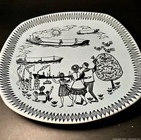 Full view of the round white ceramic plate with black graphic winter scene including dancing people, birds, ships and cranes.