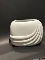 Side angle showing curved geometric ridges on matte white porcelain bisque vase.