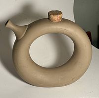 Front view of taupe bisque ceramic decanter in circular shape showing cork stopper in place.