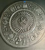 Top view of the large round glass serving platter showing central swirl pattern surrounded by detailed relief designs of berries and flowers.