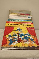Photo showing a stack of cartoon-themed vinyl records including The Smurfs, Charlie Brown, and Snoopy.