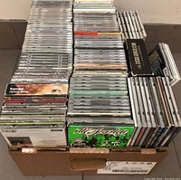 Photo of a cardboard box filled with numerous music CDs in jewel cases, stacked tightly,