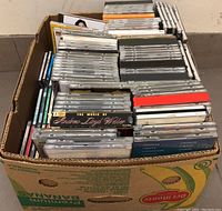 Top-down view of a cardboard box filled with over 200 CDs in jewel cases, neatly packed showing spines and some album covers.