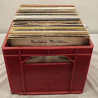 Red Borden plastic crate filled with approximately 30 vinyl LPs, showing the album titled 'Face Value Phil Collins' at the front edge