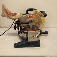 Side view of Ryobi compound miter saw showing blade, dust bag, handle and base.