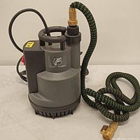Front angled view of the gray FluentPower submersible water pump with black and green hose attached and brass fitting visible.