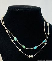 Front view of both necklaces displayed on a black bust; shows the double-strand pearl necklace and the turquoise stone necklace. Clear detail of pearl and turquoise beads.