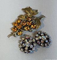 Top view of the CORO brooch and clip-on earrings laid on a light background showing details of rhinestones and metalwork.