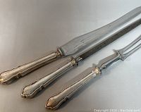 Three sterling silver handled serving cutlery pieces: knife, fork, and spoon, with detailed ornate handles.