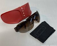 Sunglasses with red Prada case and black cleaning cloth on white surface, showing the overall lot contents