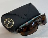 Ray-Ban sunglasses with brown lenses resting in black leather case with Ray-Ban logo and gold UV protection label