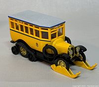 Close-up photo of yellow and black 1923 Scania-Vabis Post Bus die-cast model with skis attached, showing detailed windows, gold wheels, gray roof and spare tires mounted on sides.