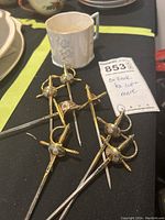 View of white porcelain teacup with floral design alongside seven small decorative swords with ornate hilts.