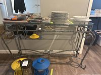 Full view of console table showing metal frame with silver and gold details, glass top, and small lower shelf with curved design.