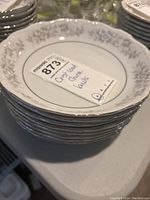 Stack of 8 white ceramic bowls with Ivy Mist gray floral pattern and scalloped rims with silver lining, some minor wear visible.