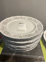 Stack of 12 white Crestwood China plates with grey Ivy Mist floral pattern on rim.