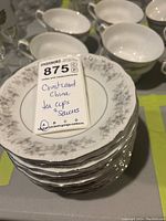 Stack of 12 Crestwood China saucers with floral pattern and tag showing lot details.