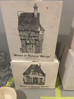 Boxes of two Department 56 Shops of Dickens Village collection items, showing detailed black and white illustration of buildings: one titled 'Smithy' and another with a house facade representing the candles shop.