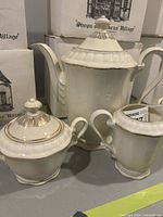 Three-piece vintage German tea set with ivory porcelain and gold trim: teapot, sugar bowl with lid, and creamer.
