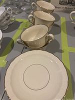 Photo showing several ivory-colored teacups with gold trim, set on a table.