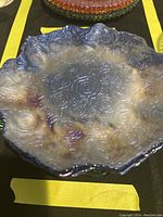 Top view of a frosted glass accent plate with scalloped edges and detailed swirl pattern, showing gradient of amber and clear colors.