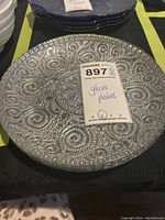 Full view of one decorative glass plate showing intricate silver swirl and dot pattern with 8 in diameter note and lot number tag
